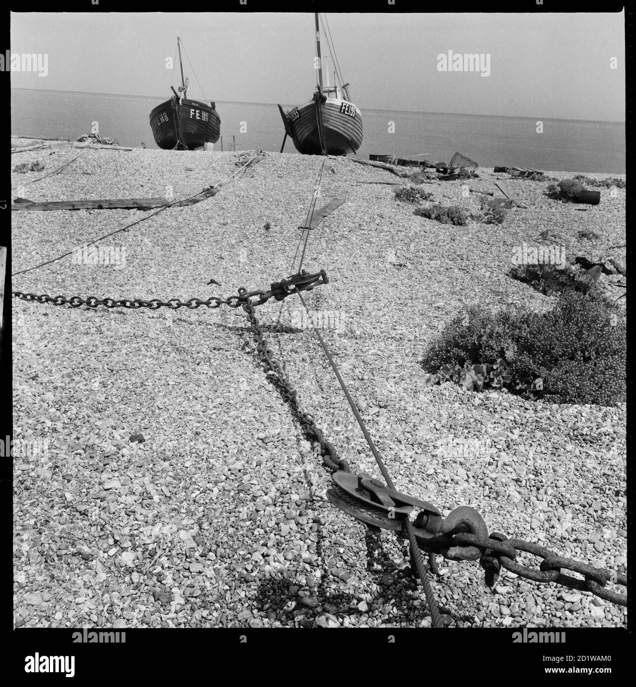 Dungeness, Lydd, Shepway, Kent. A view along the beach towards a pair of fishing boats with a winch in the foreground. Stock Photo