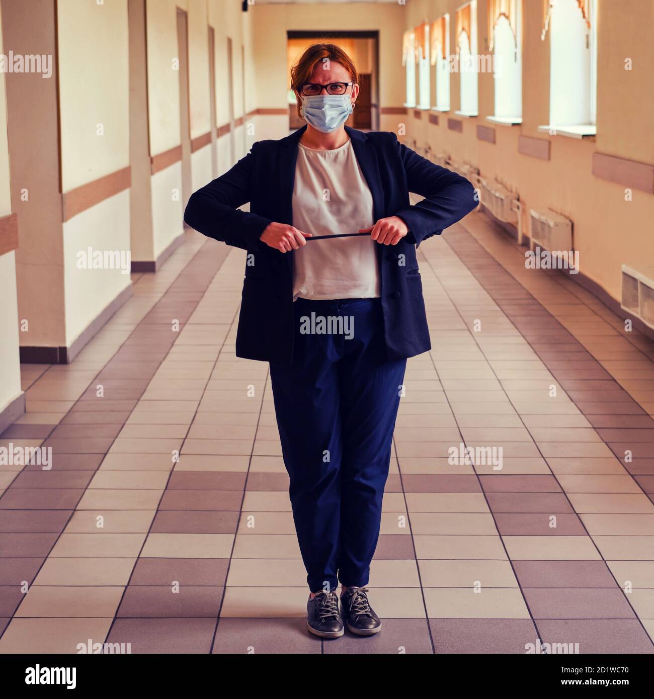 An angry teacher with a pointer in a medical mask stands in an empty ...