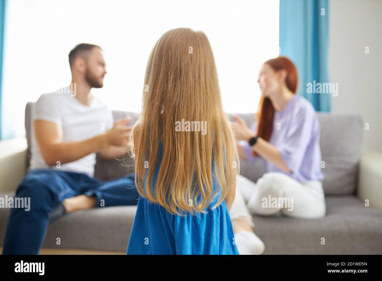 rear view on caucasian child girl looking at quarrel of parents at home, depressed redhead woman and bearded guy emotionally discuss something Stock Photo
