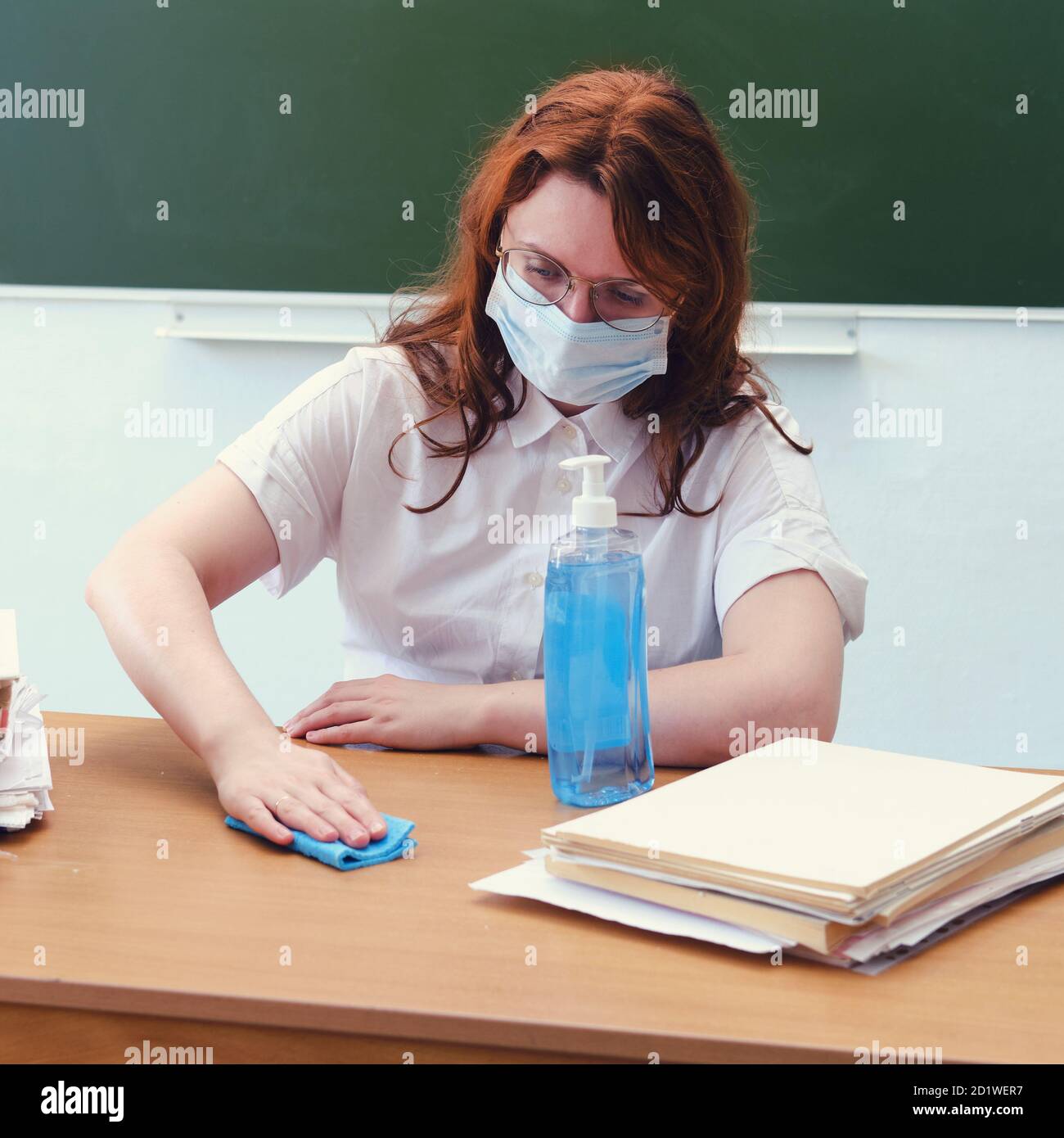 Woman teacher in medical mask wipes her desk with a rag with ...
