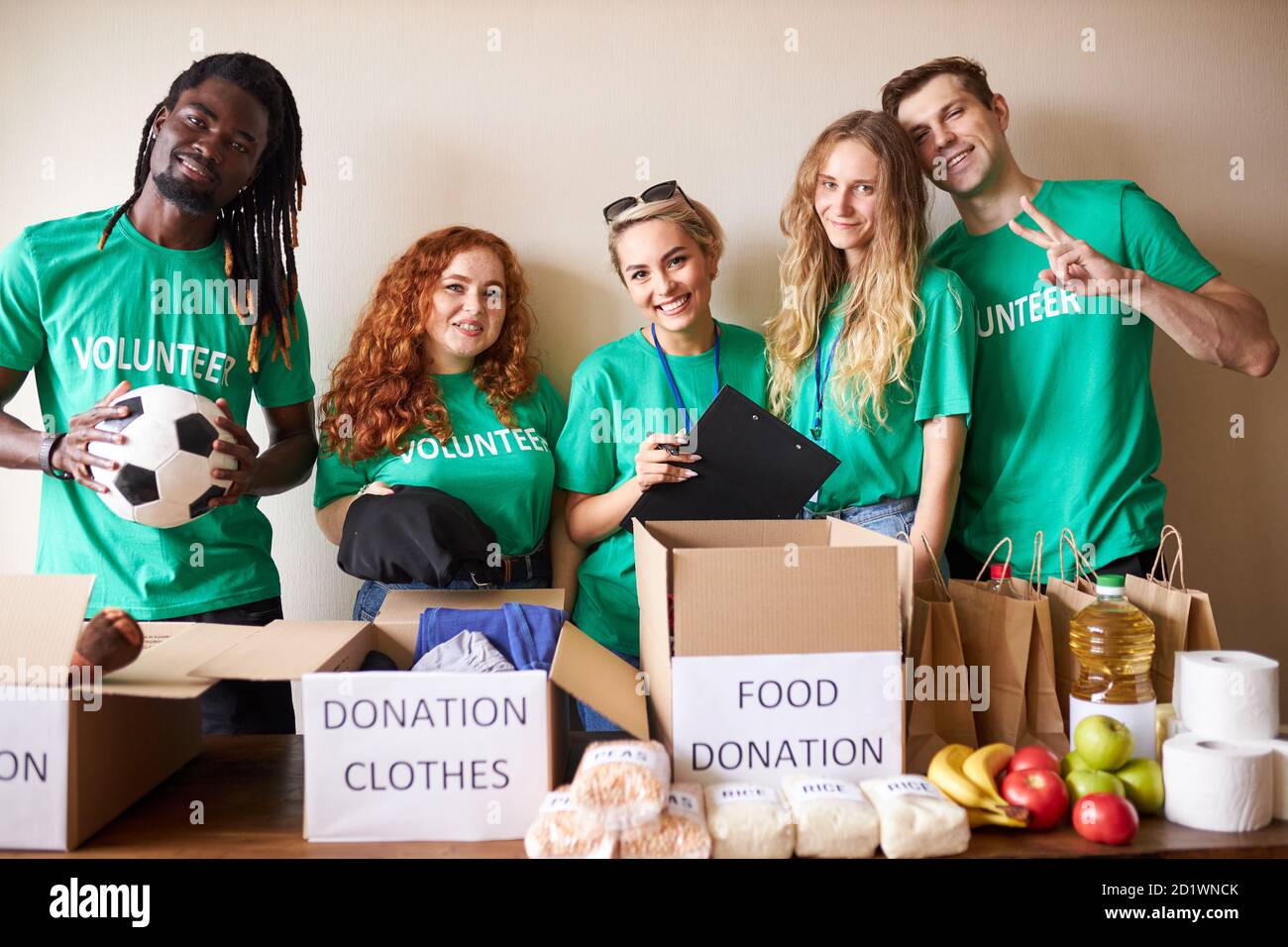 happy young volunteers donating clothes and food for charity, indoors. active ethusiastic volunteering team putting stuff into boxes for poor people. kindness and generosity concept Stock Photo