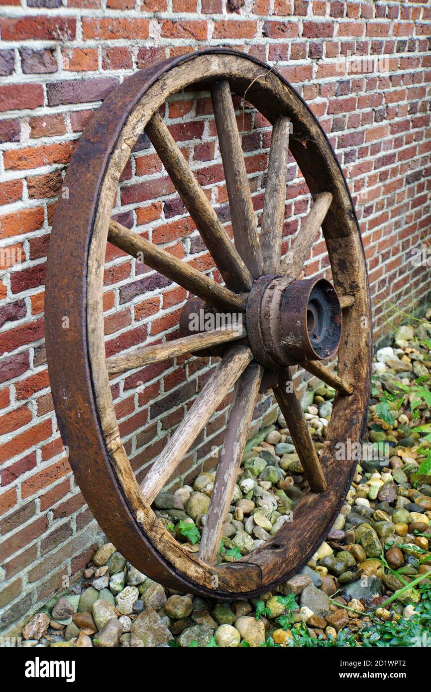 Old wooden wagon wheel with iron rim. It is placed against the wall for decoration. Stock Photo