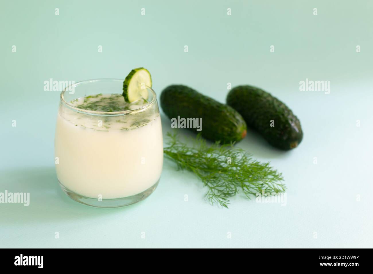 Ayran in a glass glass with a sprig of dill and cucumbers on a blue background. Fermented product concept. Copy space. Selective focus. Stock Photo