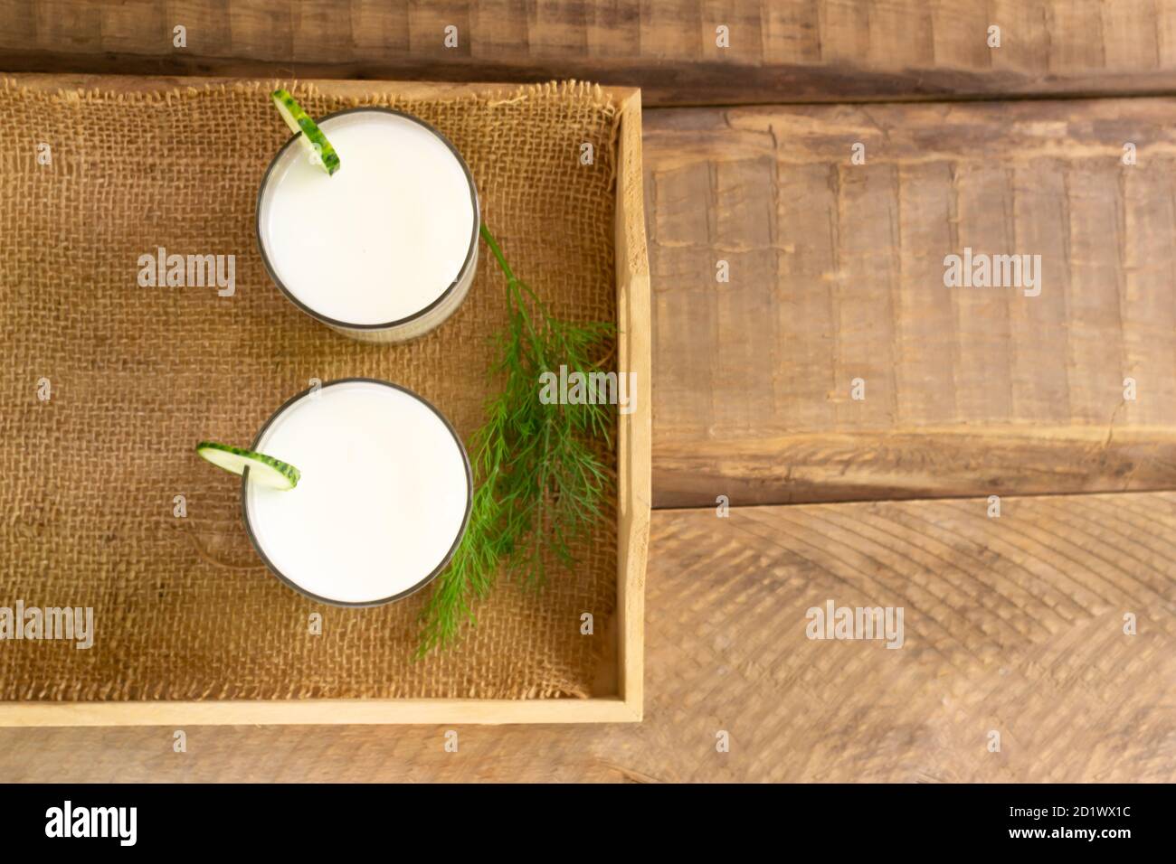 Two glasses with Ayran with cucumber on a wooden tray on a wooden background. Fermented product concept. Copy space. Top view. Stock Photo