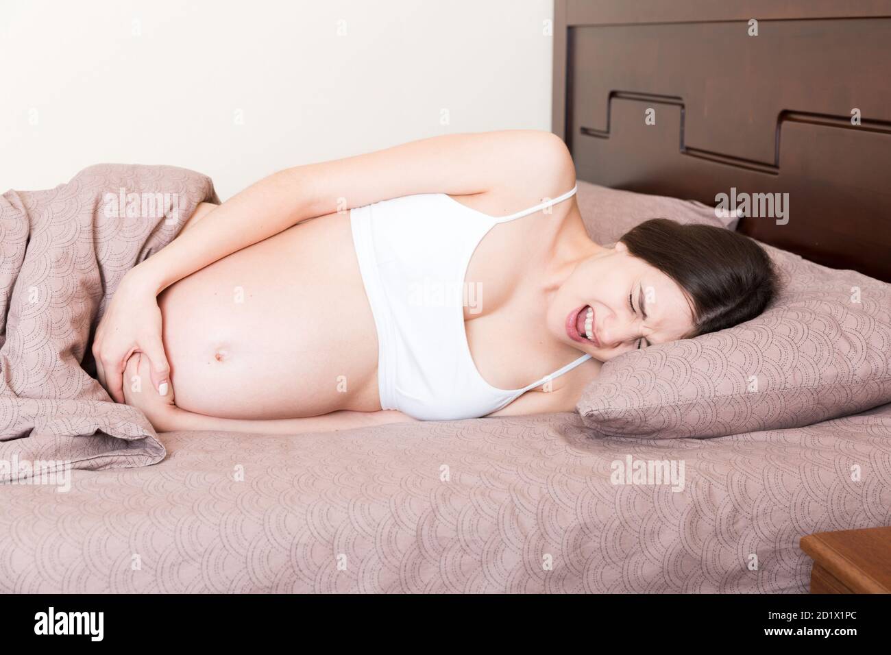 Stressed pregnant woman lying in bed with her hand on her stomach, grimacing from the bolt. Stock Photo