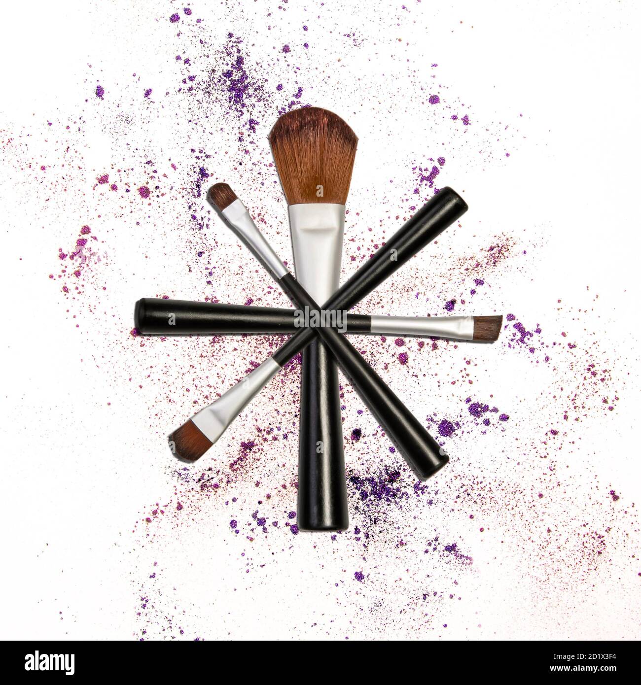 professional makeup brushes balanced in a star formation on eye shadow sparkle background in purple and pink Stock Photo