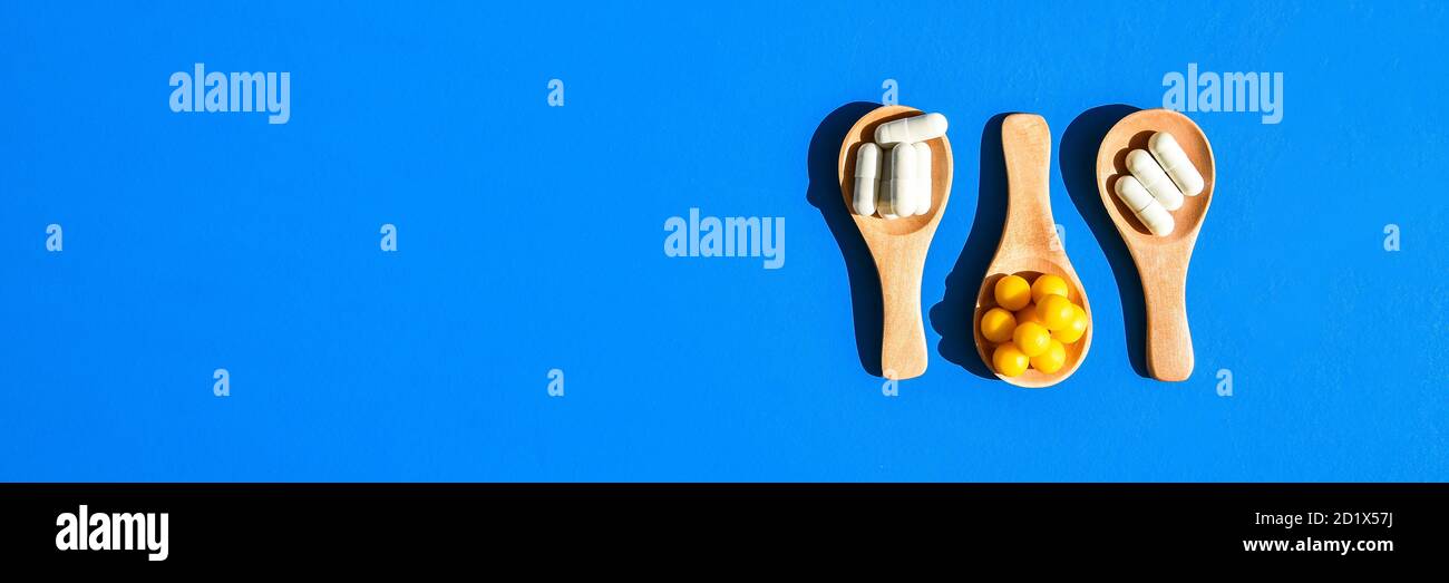 Pills and capsules on wooden spoons on blue background. Hard light and shadows. Copy space. Vitamins prebiotics probiotics. Drug dose. Stock Photo