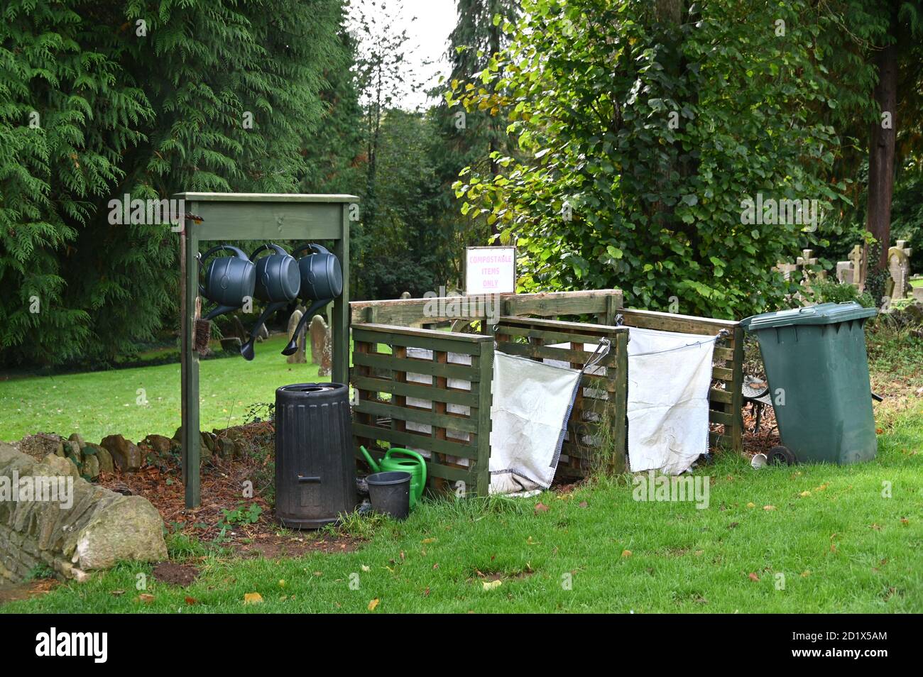 Watering cans hanging on a rack beside compost bins set up by the