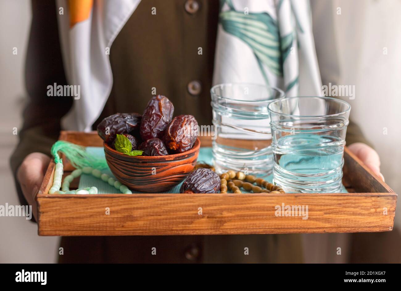 A female hand holds a tray with dates, and water and a rosary - hthe things used to break the fast at sunset during the Muslim holy month of Ramadan. Stock Photo