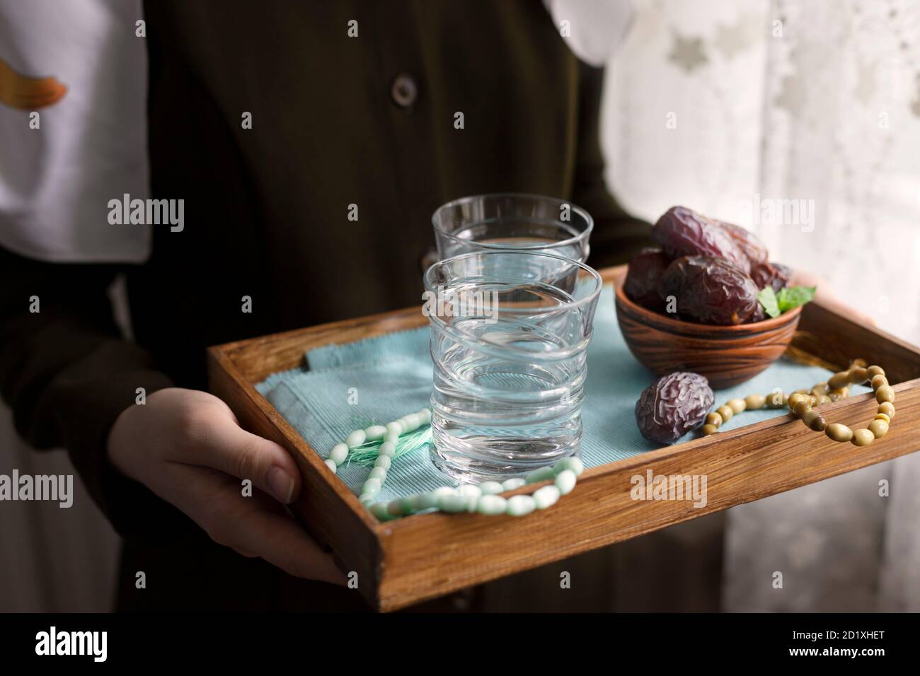 A female hand holds a tray with dates, and water and a rosary - hthe things used to break the fast at sunset during the Muslim holy month of Ramadan. Stock Photo