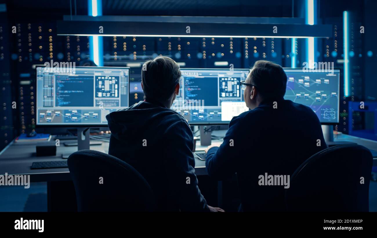 Two Professional IT Programers Discussing Blockchain Data Network Architecture Design and Development Shown on Desktop Computer Display. Working Data Stock Photo