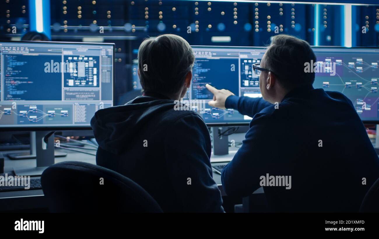 Two Professional IT Programers Discussing Blockchain Data Network Architecture Design and Development Shown on Desktop Computer Display. Working Data Stock Photo