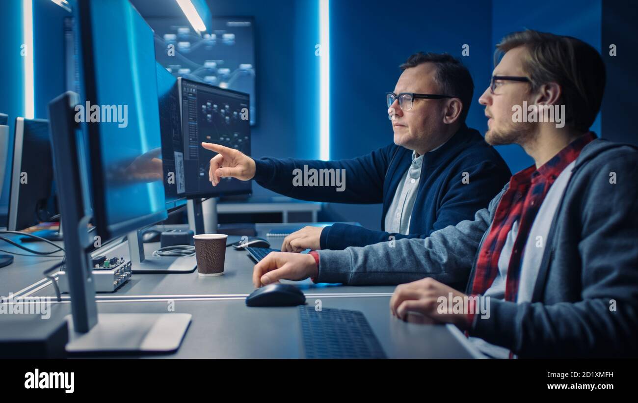 Two Professional IT Programers Discussing Blockchain Data Network Architecture Design and Development Shown on Desktop Computer Display. Working Data Stock Photo