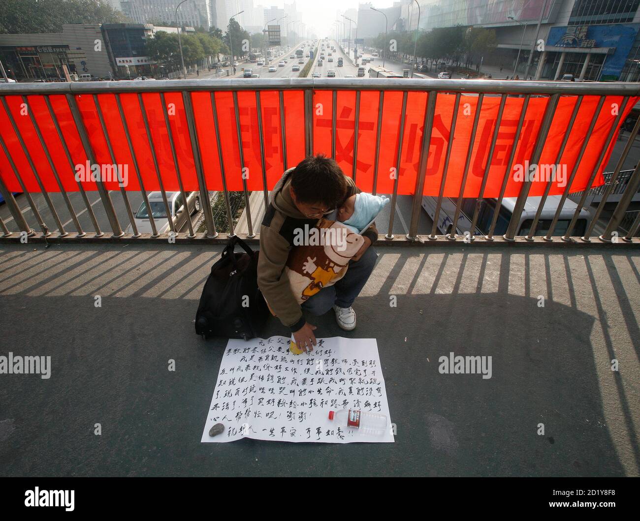 A Man Holds A Baby As He Sits In Front Of A Poster On A Walkway Bridge Above A Main Road In Beijing November 5 08 The Poster Describes His Plight In