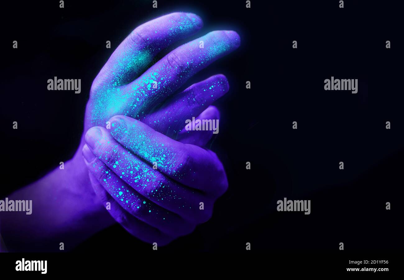Washing hands in UV ultra violet light illustrating bacteria and viruses on hands and the importance of good hygiene. Covid 19 pandemic concept. Stock Photo