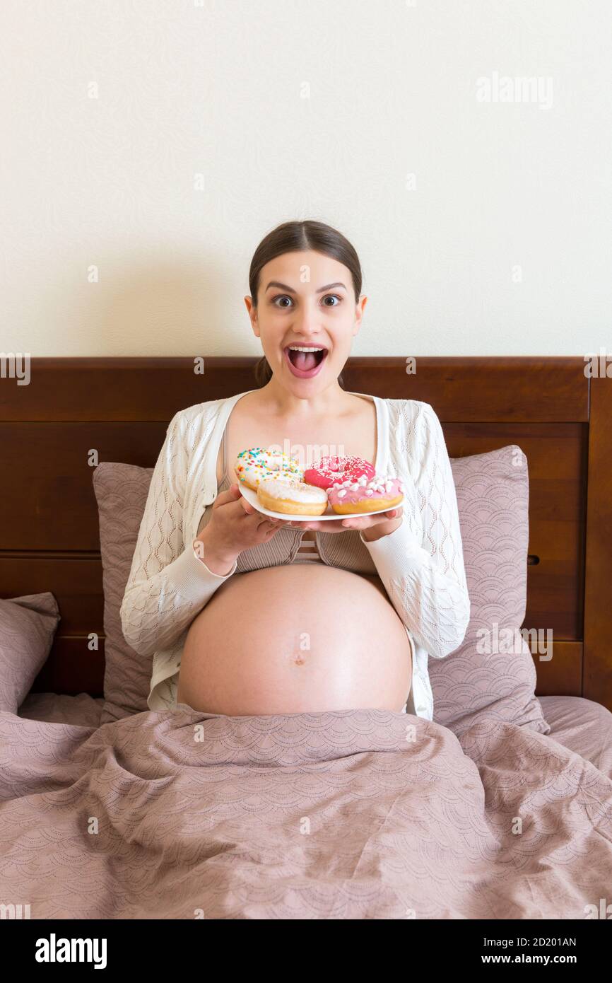 Pregnant woman is eating many donuts relaxing in bed. Unhealthy dieting