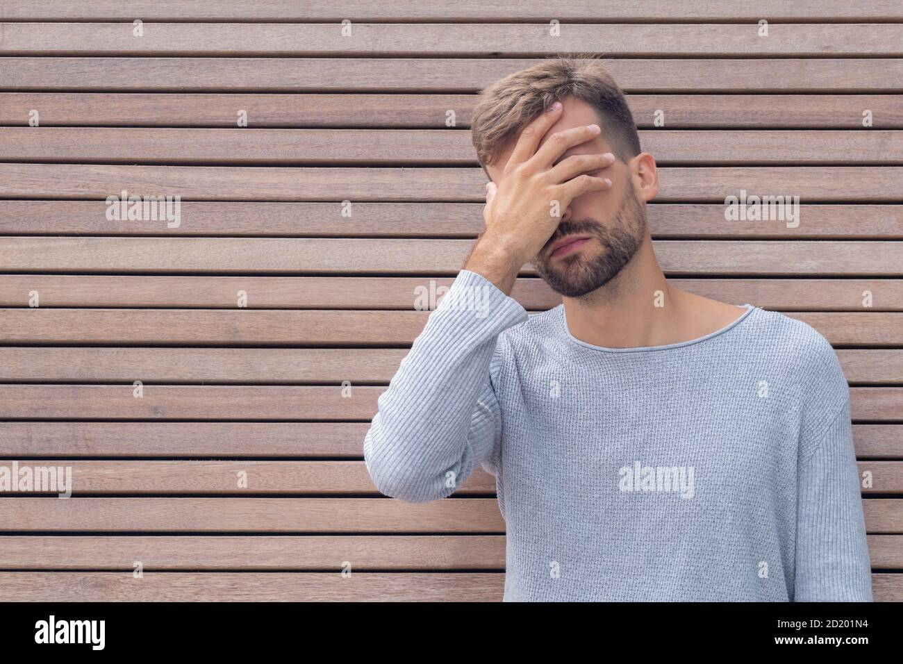 Facepalm. Ashamed embarrassed man covering his face. Young guy on wooden wall background with copy space. Emotion facial expression and feelings conce Stock Photo