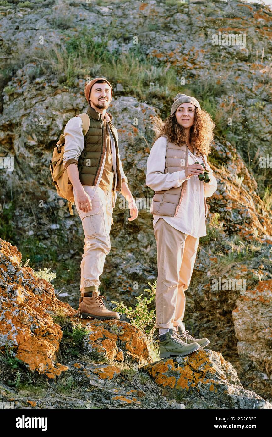 Content active young couple in comfortable wear walking over stone rocks while hiking together Stock Photo