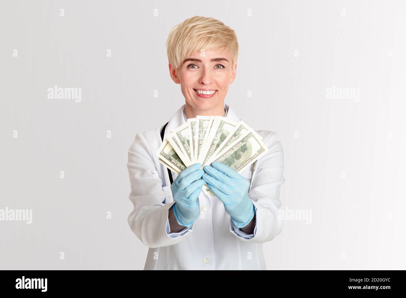 Corruption of medical system. Happy female doctor in white coat and rubber gloves received money and shows dollars Stock Photo