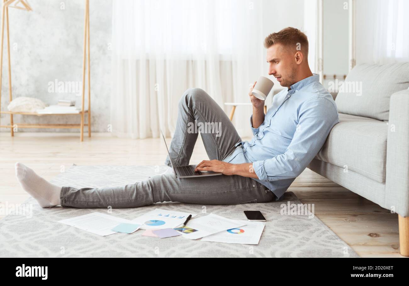 Focused man sitting on floor using phone drinking coffee Stock Photo