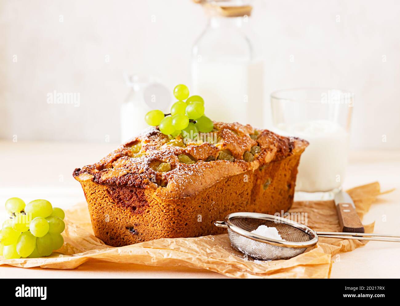 Delicious homemade grape loaf cake with thyme and sugar powder on parchment paper. Light stone background. Stock Photo
