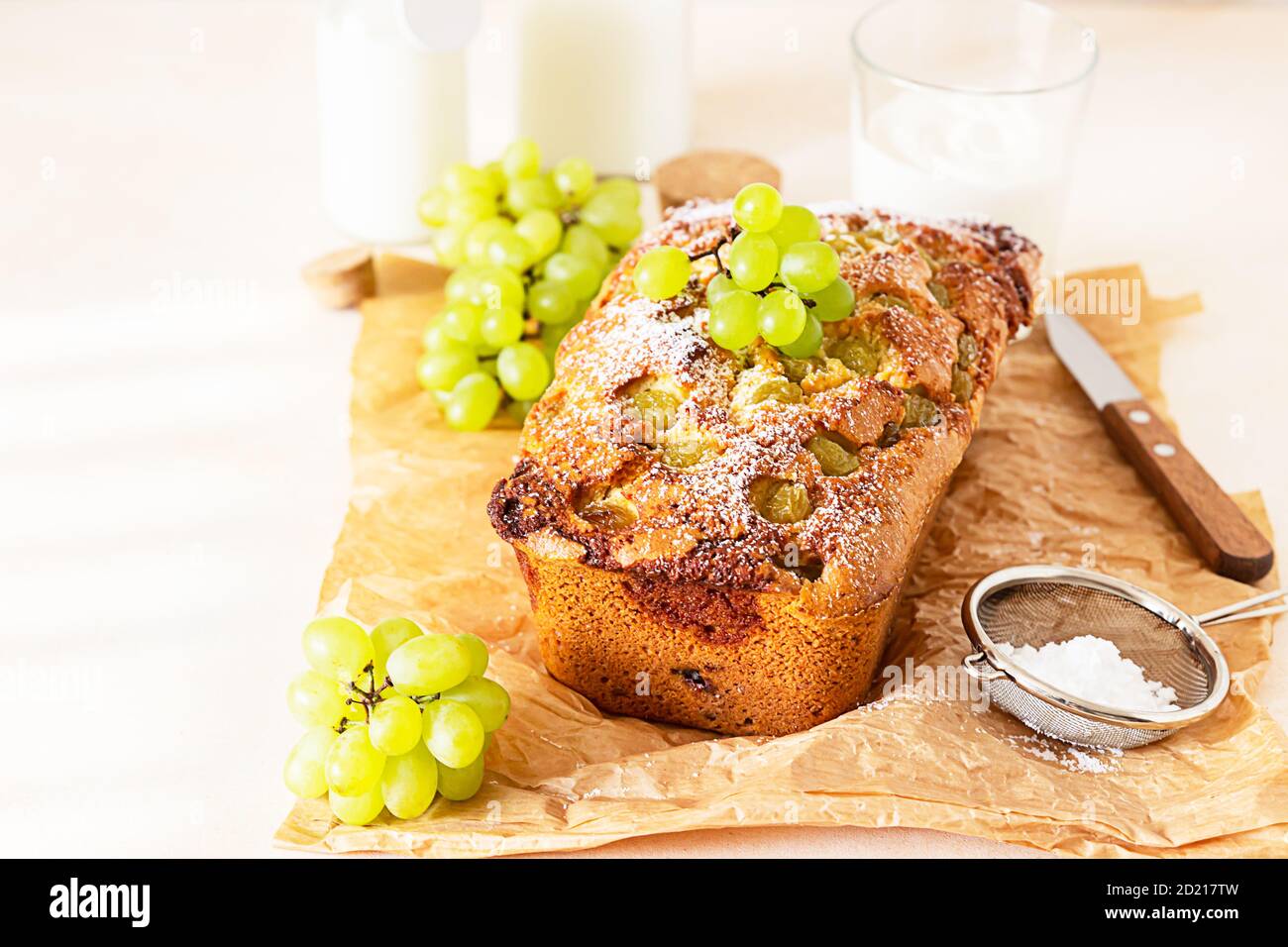 Delicious homemade grape loaf cake with thyme and sugar powder on parchment paper. Light stone background. Stock Photo