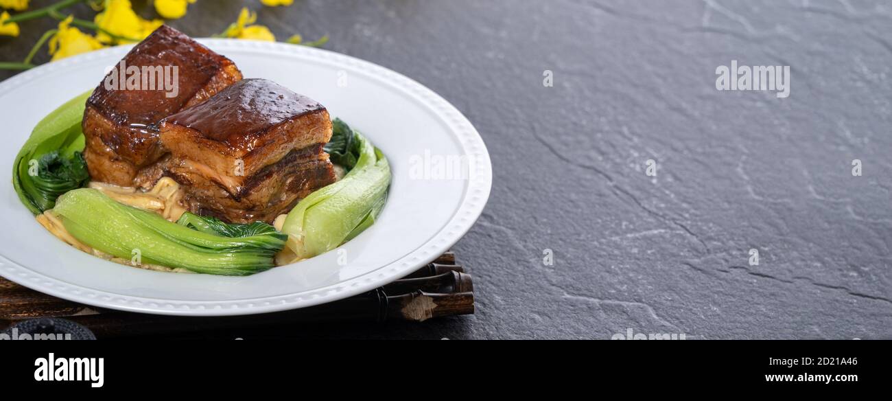 Dong Po Rou (Dongpo pork meat) in a beautiful plate with green vegetable, traditional festive food for Chinese new year cuisine meal, close up. Stock Photo