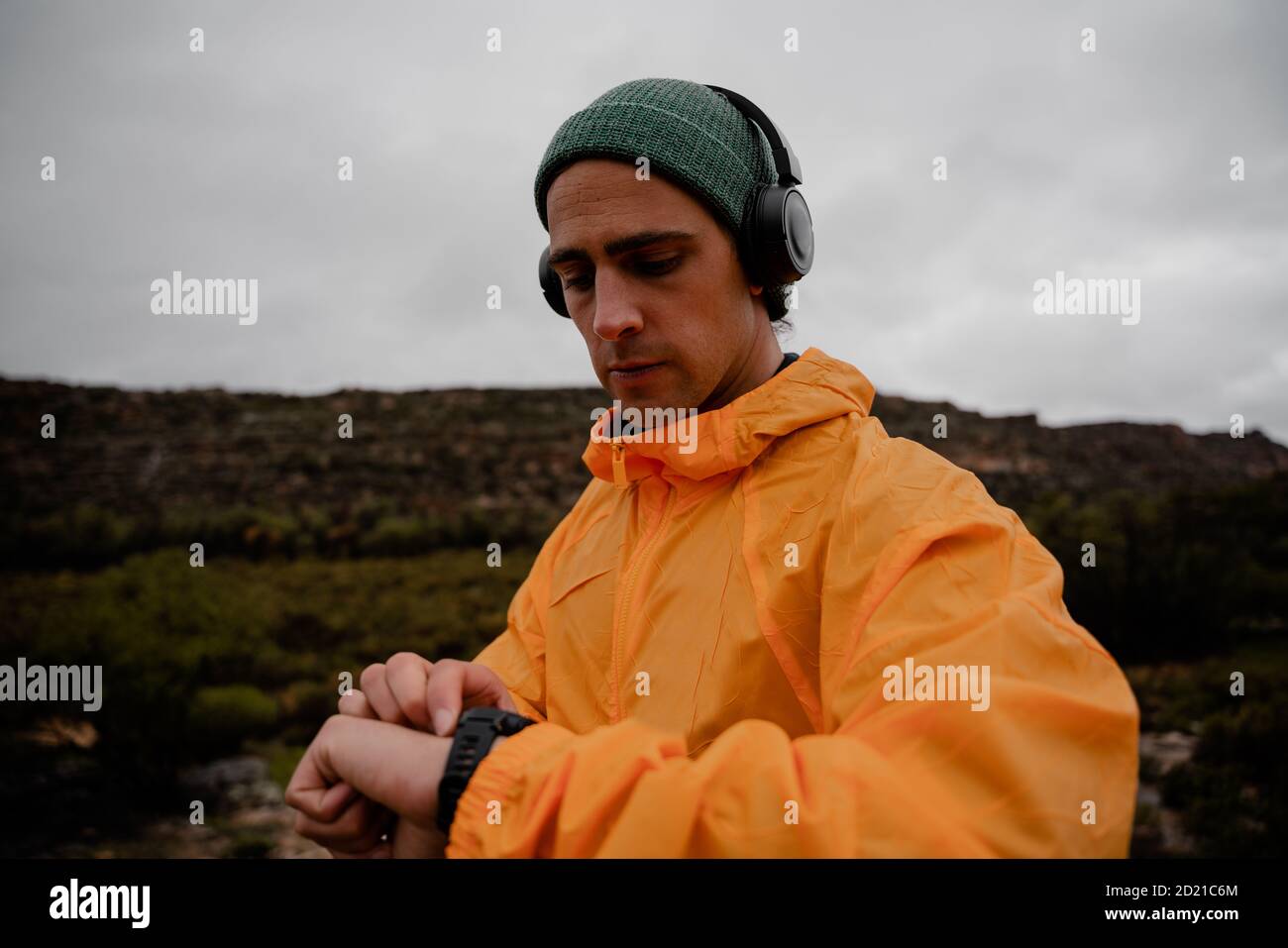 Fit young male athlete setting up smartwatch to track activity listening to music in headphones on run on mountain path Stock Photo