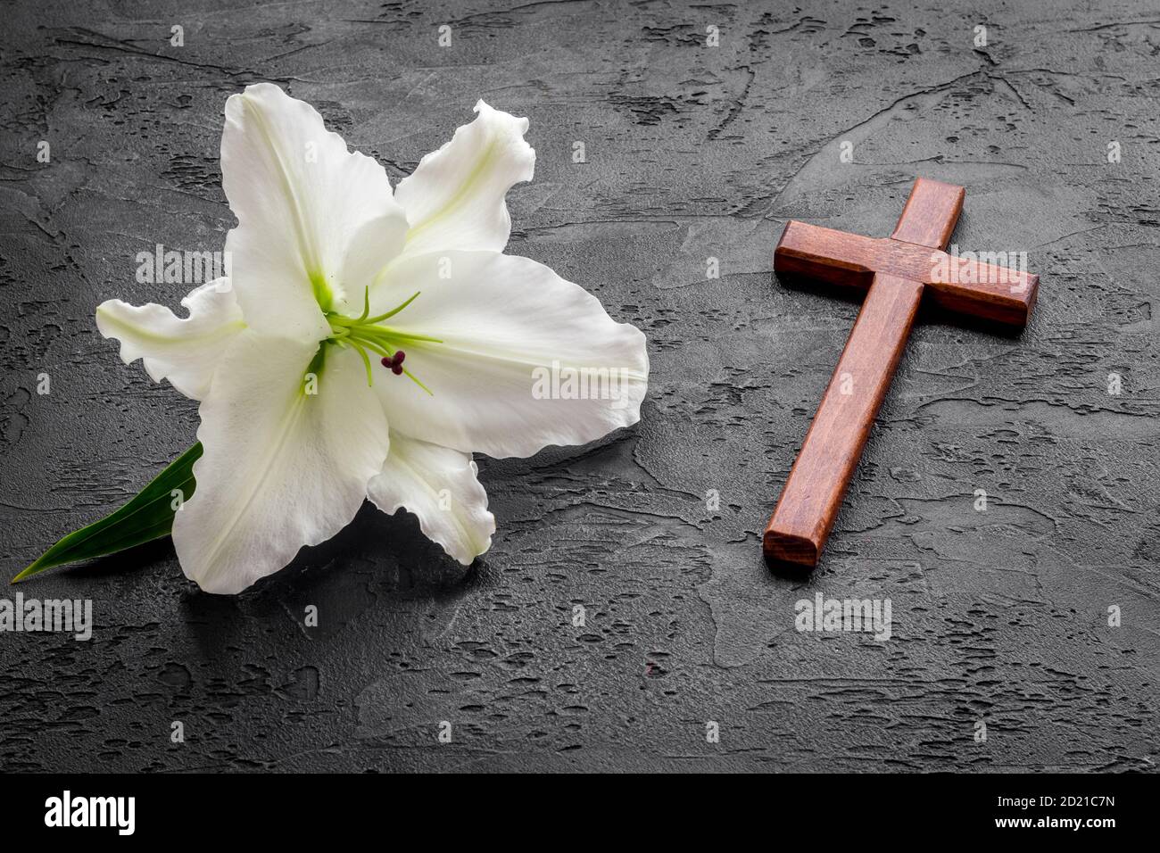 Funeral lily flowers with cross on dark stone background. Mourning