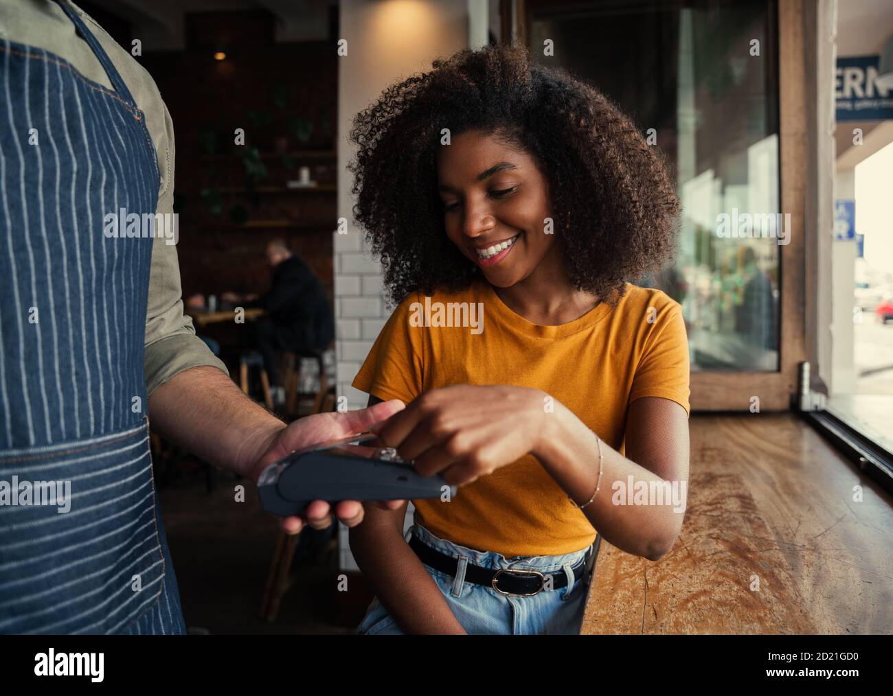 Smiling mixed race woman with afro happily paying for coffee at coffee shop. Stock Photo