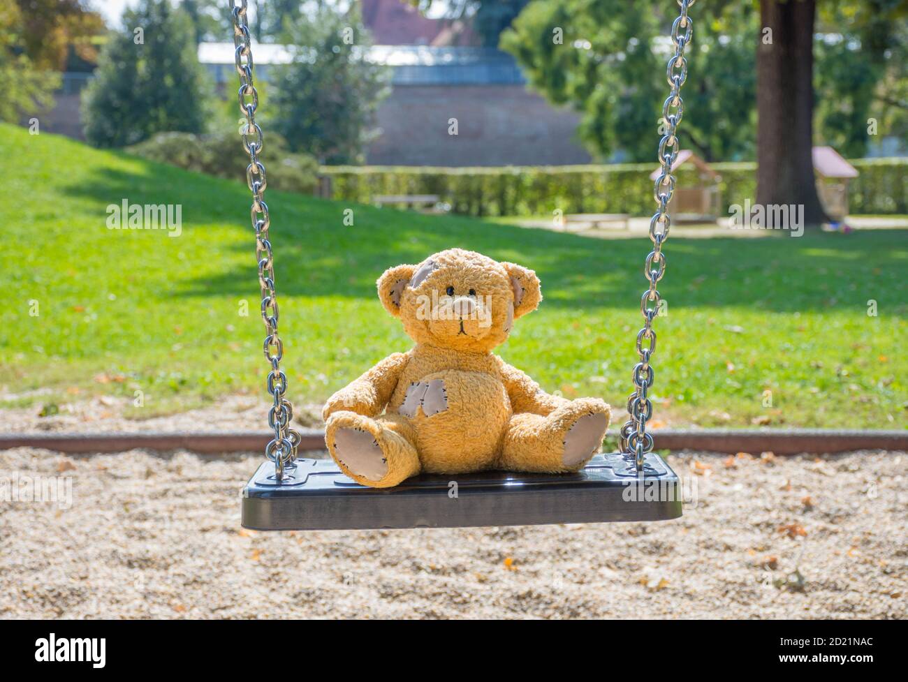 Cute little teddy bear standing alone on a swing in empty park on a ...
