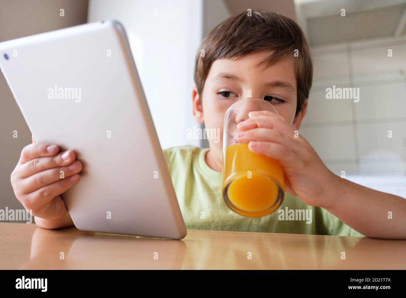 Boy in the kitchen drinking orange juice and watching video on the tablet Stock Photo - Alamy