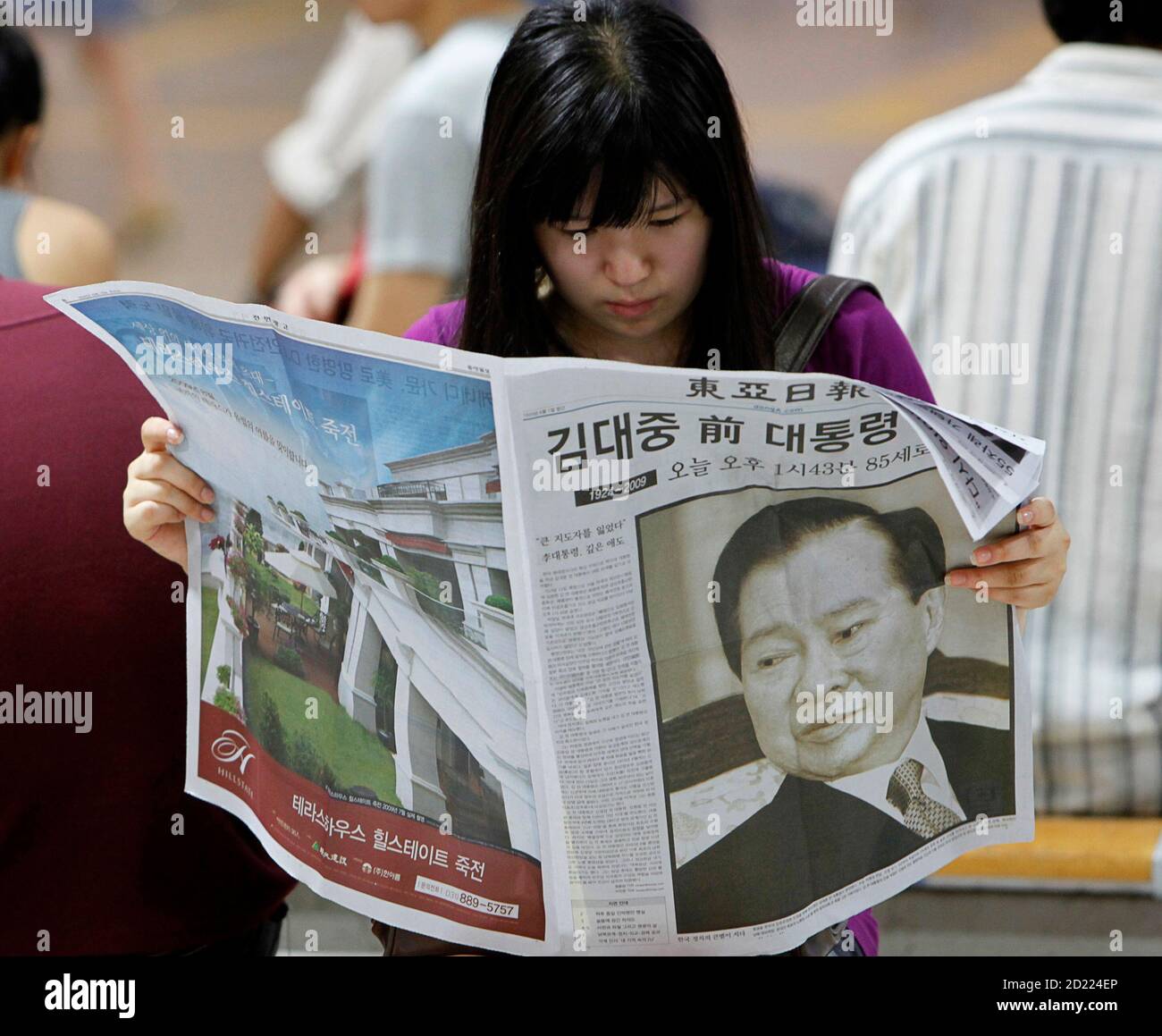 A woman reads an extra edition of a newspaper reporting on former South Korean President Kim Dae-jung's death at the Seoul railway station August 18, 2009. Former South Korean President Kim, a towering figure in South Korea's struggle for democracy who won the 2000 Nobel Peace Prize for seeking rapprochement with the communist North, died on Tuesday at the age of 85. An official at a Seoul hospital treating Kim for pneumonia confirmed the death.  REUTERS/Jo Yong-Hak (SOUTH KOREA POLITICS OBITUARY) Stock Photo