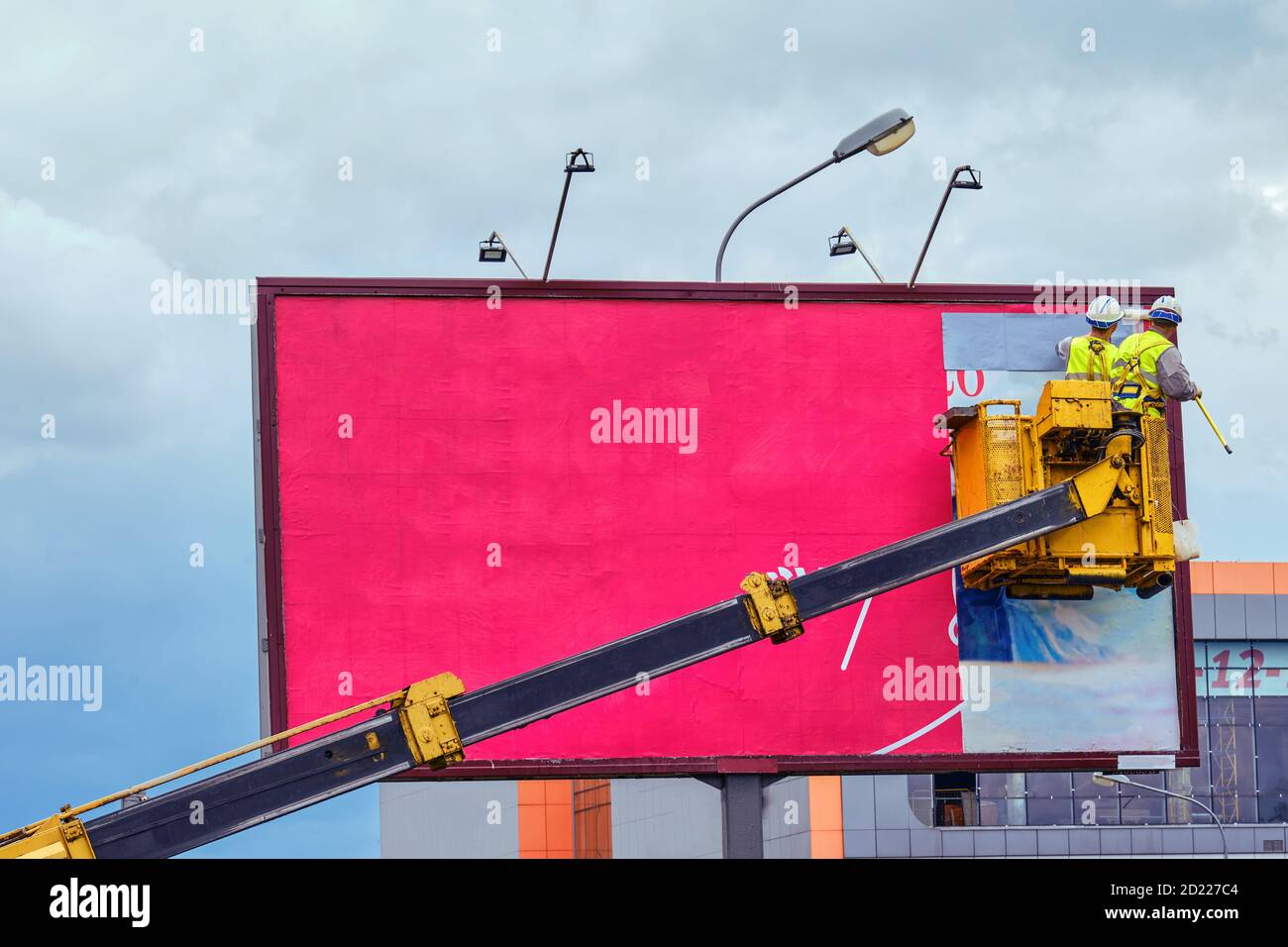 Two workers install red billboard on roadside of city street Stock Photo