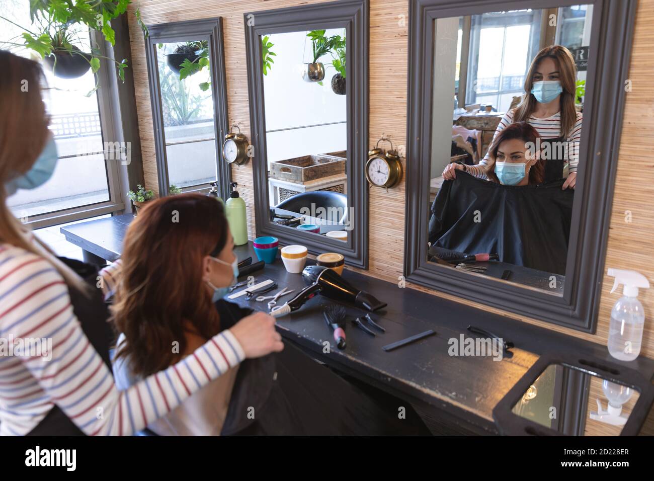 Female hairdresser wearing face mask putting cape on female customer at