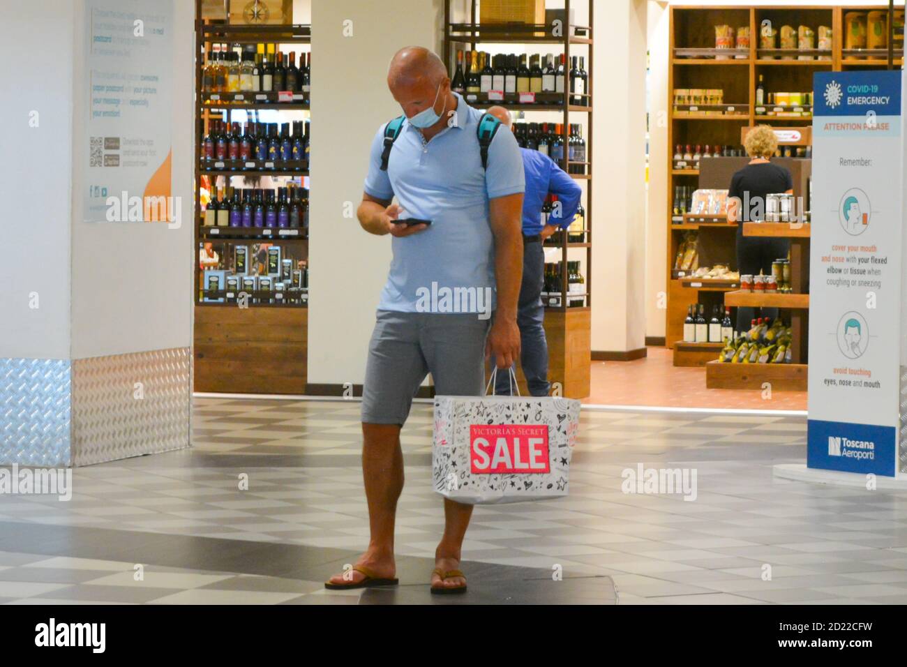 Man, tourist wearing coronavirus protection mask with a shopping bag stending in front of a wine and duty free shop at the airport, Business crisis Stock Photo