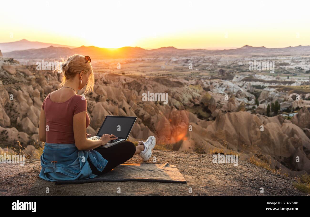 Young girl working at laptop at sunset on top of mountain with beautiful view at valley Stock Photo