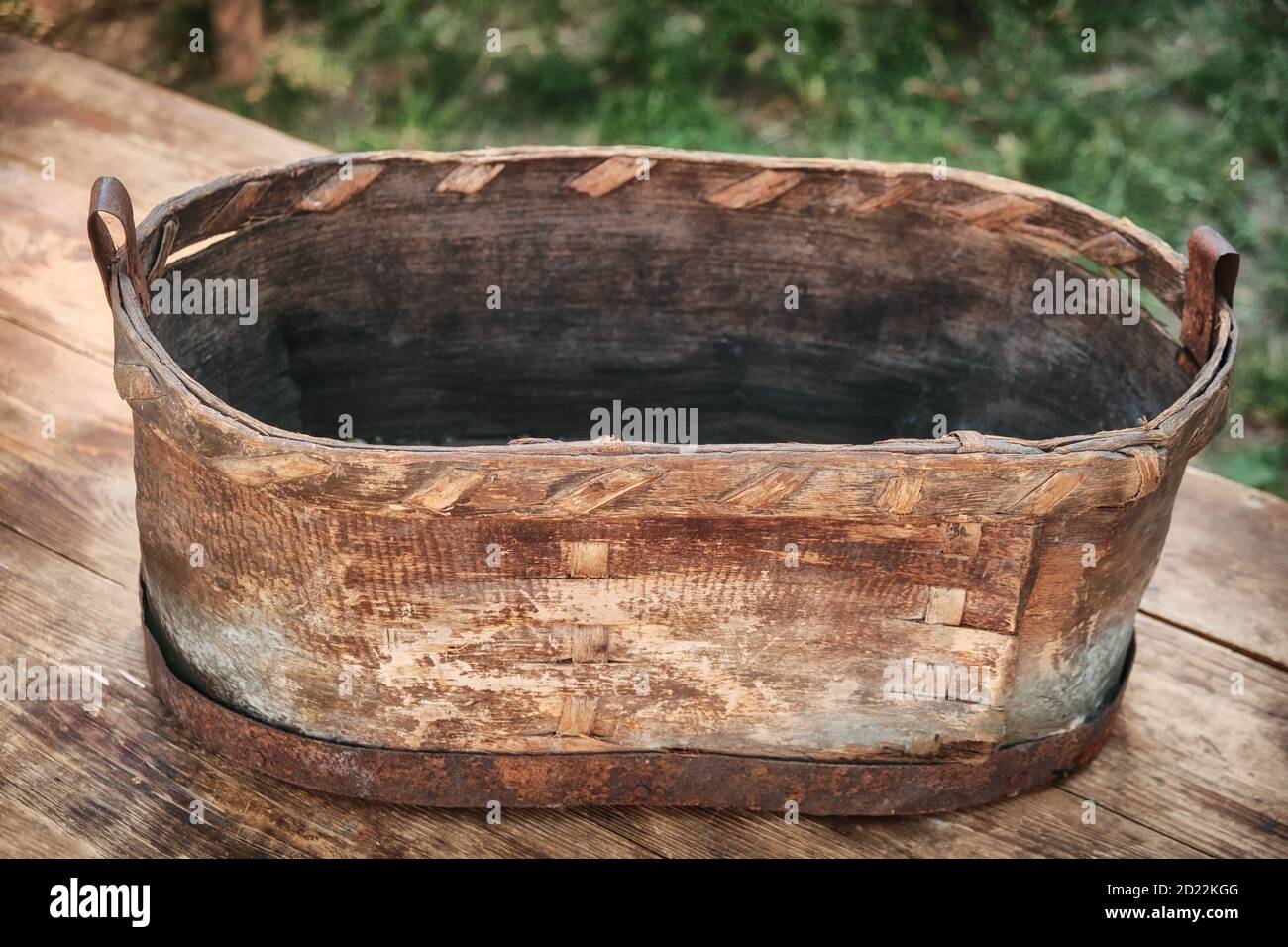 An old trough made from the bark of a tree. Vintage washtub woven from wood, with a metal rim at the bottom. Stock Photo