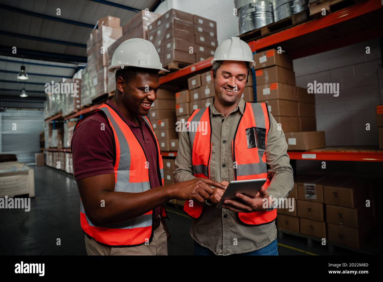 Smiling workers browsing on digital tablet watching funny videos standing in factory  Stock Photo