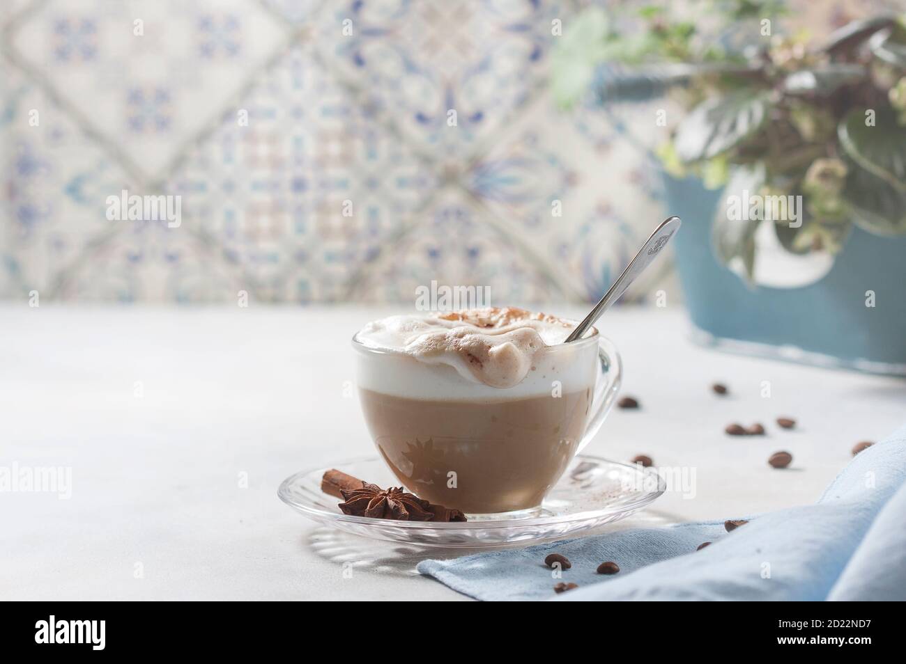 Cappuccino or latte in a glass cup on a light background. Female hand with a spoon Stock Photo