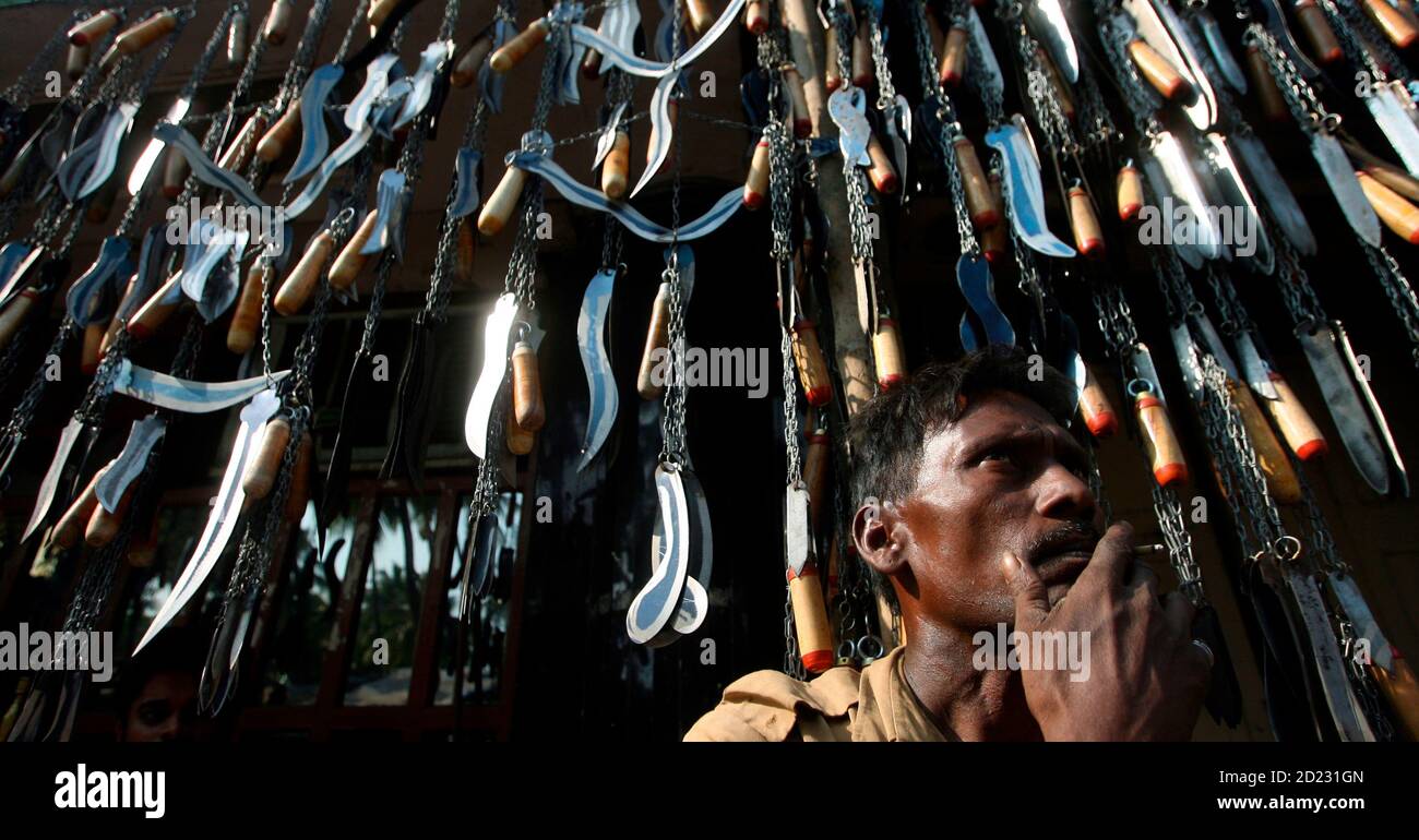 A man smokes 'bidi', an Indian leaf cigarette, in front of blades on chains, to be used for self-flagellation rituals during the Shi'ite festival of Ashura, displayed for sale in Mumbai December 7, 2009. Ashura, a 10-day period of mourning in the Islamic month of Muharram, commemorates the death of Imam Hussein, Prophet Mohammad's grandson, in the 7th century battle of Kerbala. REUTERS/Arko Datta (INDIA) Stock Photo