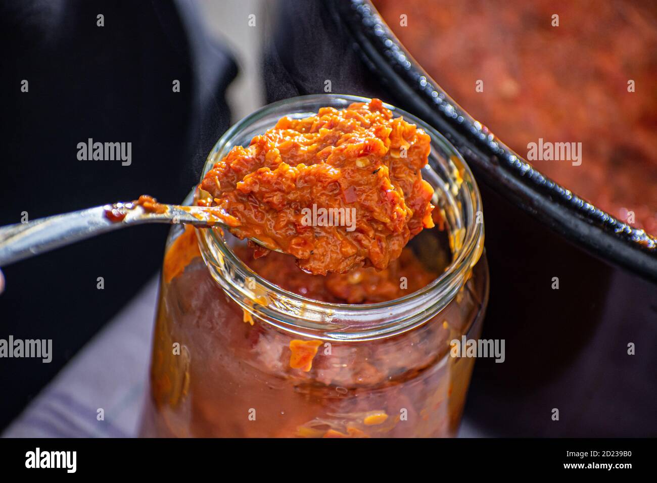 pouring fresly cooked ajvar into the jar with spoon Stock Photo