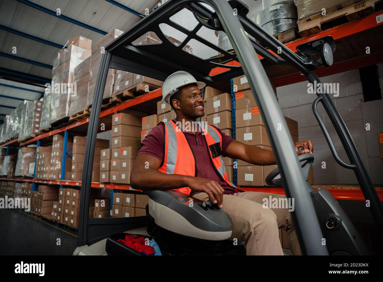 Mixed race worker driving forklift around warehouse while searching for parcels  Stock Photo