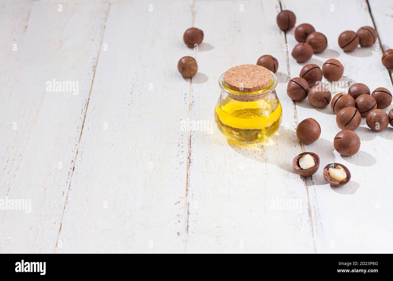Natural macadamia oil and Macadamia nuts on wooden white board. Healthy product. Healthy food concept. Stock Photo