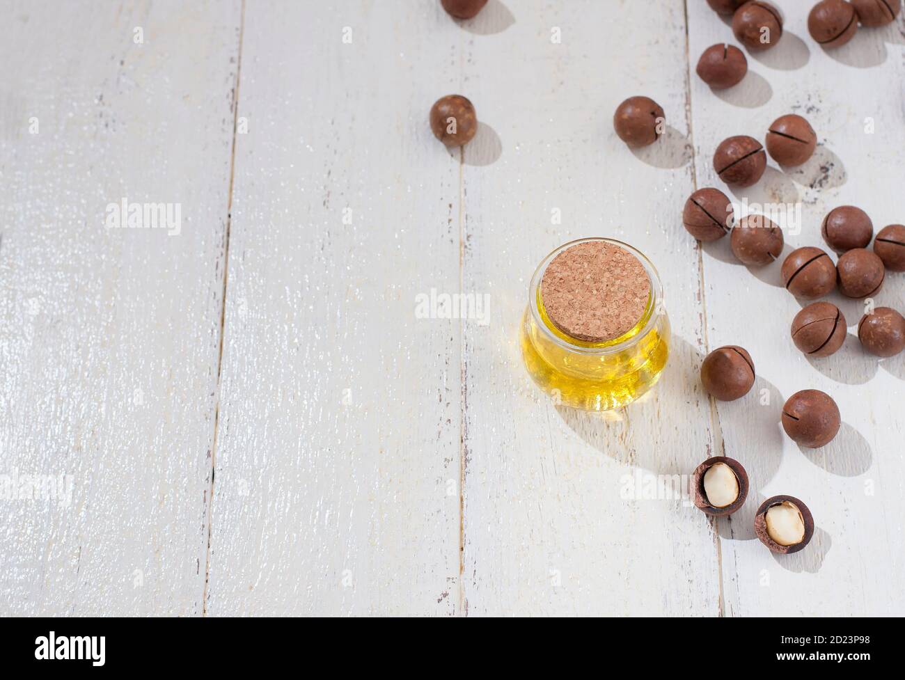 Natural macadamia oil and Macadamia nuts on wooden white board. Healthy product. Healthy food concept. Stock Photo