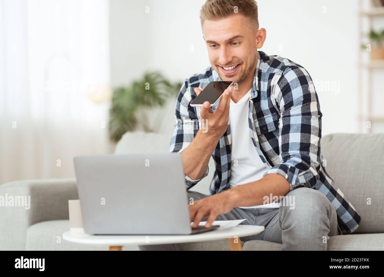 Young man using voice assistant on his cellphone, using pc Stock Photo