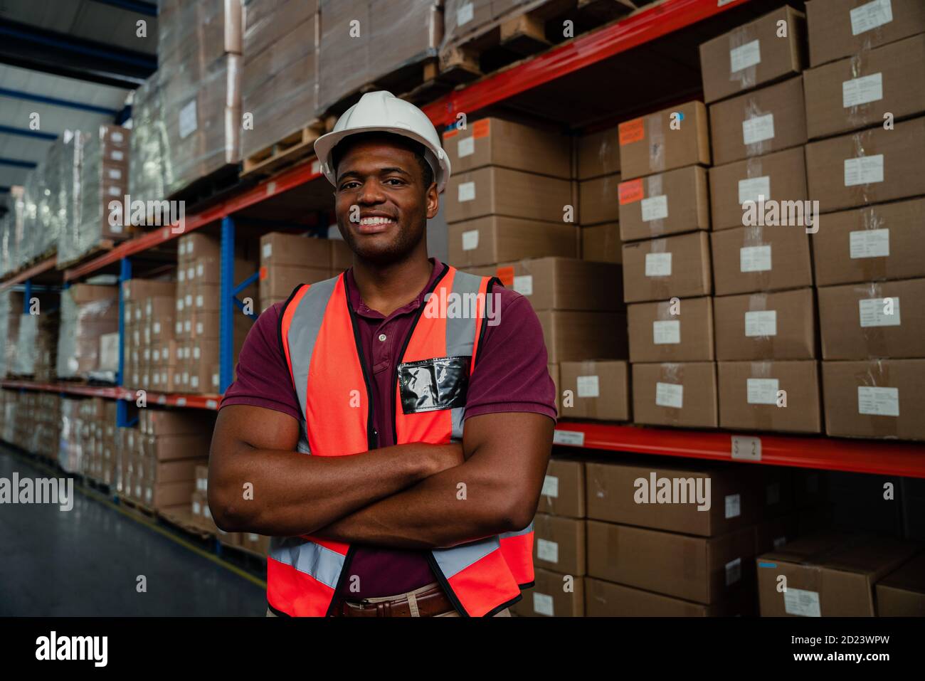 Smiling mixed race worker standing besides parcels in warehouse. Stock Photo
