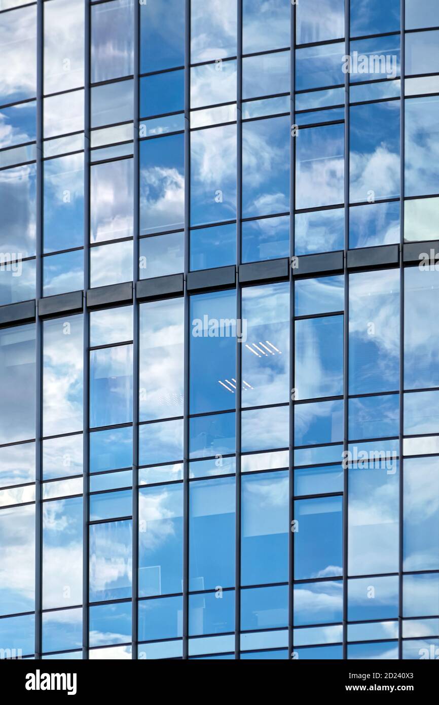 Windows of a skyscraper with reflection of blue sky and white clouds. A ...