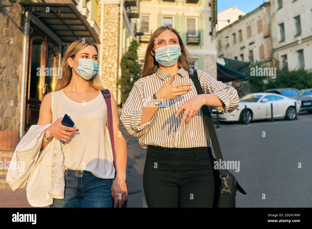 Two young business women in protective medical masks walking together ...