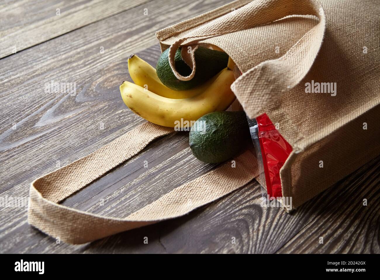 Reusable shopping bag with fresh fruits. Natural eco friendly material. Products from the store. Yellow bananas, green avocado, hessian or jute sack o Stock Photo